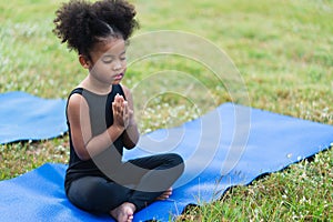 African American little girl sitting on the roll mat practicing meditate yoga in the park outdoor
