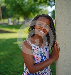 African-American little girl smiling in a garden surrounded by greenery under sunlight