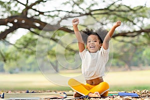 African american little girl smiling and raises her hand while sitting in the park