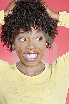 African American looking sideways with hands in hair over colored background