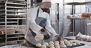 African american male baker working in bakery kitchen, spraying rolls in slow motion