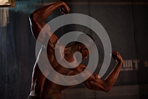 African American male body builder posing on a black background in studio setting. Back view