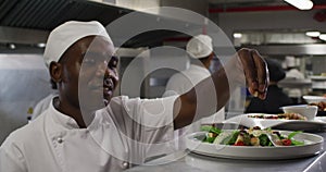 African american male chef garnishing dish and similing in restaurant kitchen