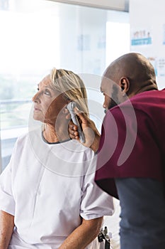 African american male doctor examining senior female caucasian patient using otoscopy