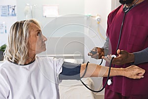 African american male doctor measuring blood pressure of senior female caucasian patient