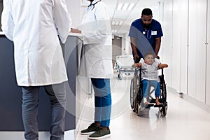 African american male doctor pushing boy patient in wheelchair in busy hospital corridor