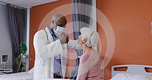 African american male doctor using penlight examining the eyes of senior caucasian female patient
