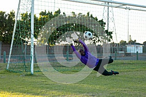 African american male goalkeeper with arms raised catching soccer ball in mid-air during match