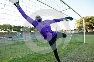 African american male goalkeeper with arms raised jumping and catching soccer ball during match