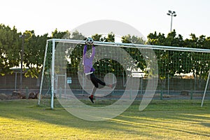 African american male goalkeeper with arms raised jumping and catching soccer ball in mid-air