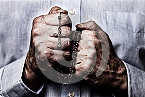 African American male hands praying holding a beads rosary with Jesus Christ in the cross or Crucifix