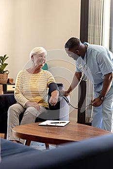 African american male health worker checking blood pressure of caucasian senior woman at home