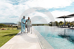 African american male health worker helping caucasian senior woman to walk with a walking frame