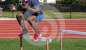 African American male jumping over track hurdles at practice