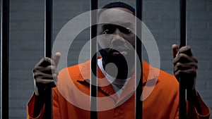 African-american male prisoner holding bars and looking to camera, imprisonment photo