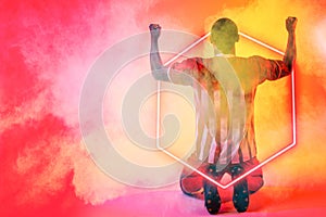 African american male soccer player with arms raised kneeling by illuminated hexagon