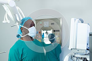 African american male surgeon studying computerised medical equipment in operating theatre