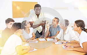 African american male teacher, together with students of different ages, conducts intensive classes at round table in