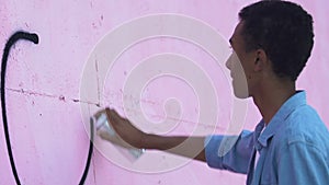 African-American male teenager painting piece sign on city wall, graffiti