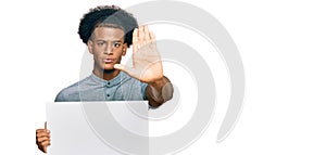 African american man with afro hair holding blank empty banner with open hand doing stop sign with serious and confident