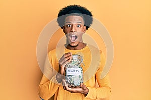 African american man with afro hair holding charity jar with money celebrating crazy and amazed for success with open eyes