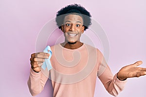 African american man with afro hair holding pink cancer ribbon celebrating achievement with happy smile and winner expression with