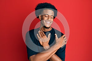 African american man with afro hair wearing casual clothes hugging oneself happy and positive, smiling confident