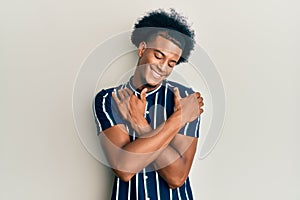 African american man with afro hair wearing casual clothes hugging oneself happy and positive, smiling confident