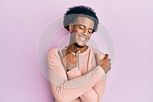 African american man with afro hair wearing casual clothes hugging oneself happy and positive, smiling confident