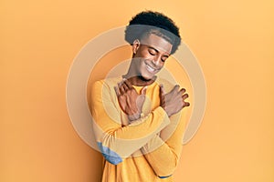 African american man with afro hair wearing casual clothes hugging oneself happy and positive, smiling confident