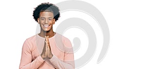 African american man with afro hair wearing casual clothes praying with hands together asking for forgiveness smiling confident