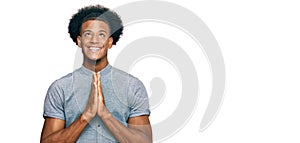 African american man with afro hair wearing casual clothes praying with hands together asking for forgiveness smiling confident