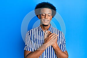 African american man with afro hair wearing casual clothes smiling with hands on chest, eyes closed with grateful gesture on face