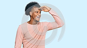 African american man with afro hair wearing casual clothes very happy and smiling looking far away with hand over head