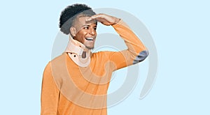 African american man with afro hair wearing cervical neck collar very happy and smiling looking far away with hand over head