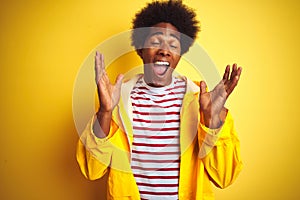 African american man with afro hair wearing rain coat standing over isolated yellow background celebrating mad and crazy for