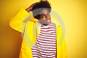 African american man with afro hair wearing rain coat standing over isolated yellow background confuse and wonder about question