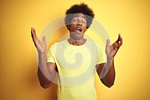 African american man with afro hair wearing t-shirt standing over isolated yellow background celebrating mad and crazy for success