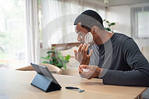 African American man applying cream on his face and using digital tablet pretend to be mirror before shaving his beard