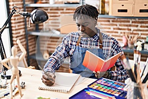 African american man artist drawing on notebook reading book at art studio