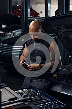 African American man auto-mechanic leaning on car choosing proper socket