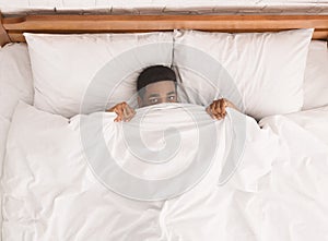 African-american man in bed hiding under blanket