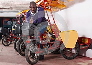 African-American man bikecab driver standing near rickshaw cycle