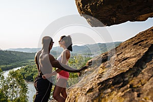 African american man bodybuilder and brunette woman in sportswear embracing on the rocky mountains background