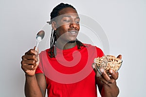 African american man with braids eating healthy whole grain celears with spoon smiling looking to the side and staring away