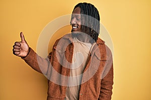 African american man with braids wearing brown retro jacket looking proud, smiling doing thumbs up gesture to the side