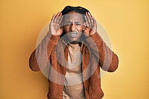 African american man with braids wearing brown retro jacket trying to hear both hands on ear gesture, curious for gossip