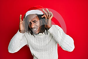 African american man with braids wearing christmas hat trying to hear both hands on ear gesture, curious for gossip
