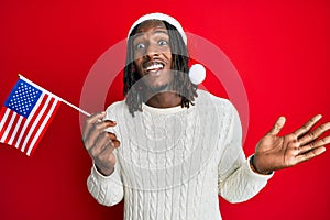 African american man with braids wearing christmas hat and usa flag celebrating achievement with happy smile and winner expression