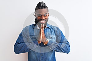 African american man with braids wearing denim shirt over isolated white background praying with hands together asking for